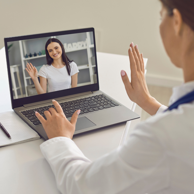A person on a laptop waves to their therapist through the screen at a virtual therapy appointment.