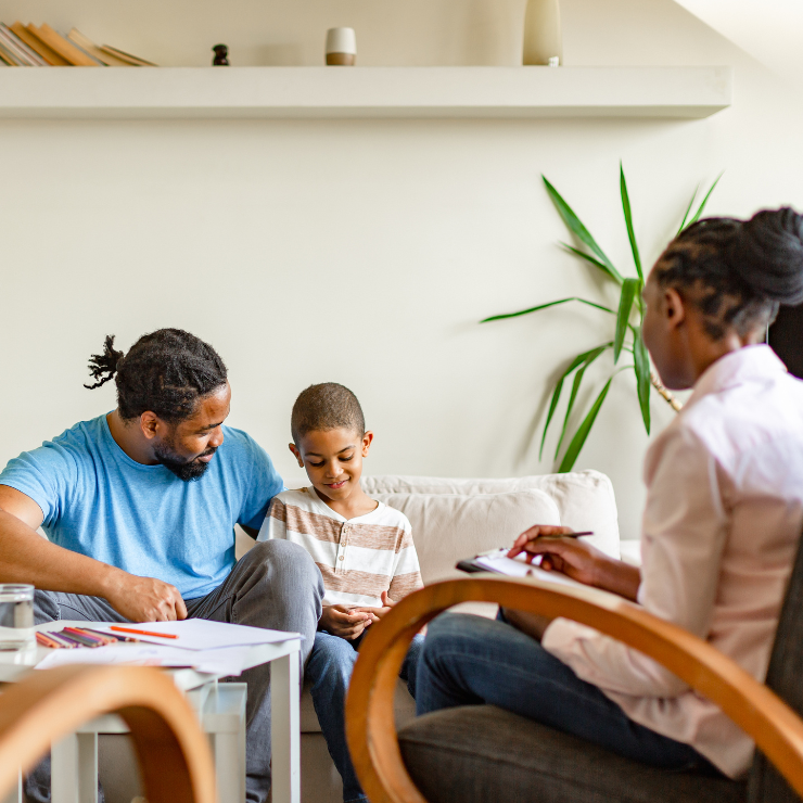 A parent and child sit on a couch facing a therapist in a chiar.